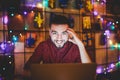 A young handsome Caucasian man with beard and toothy smile in a red checkered shirt is working behind a gray laptop sitting at a w Royalty Free Stock Photo