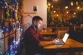 A young handsome Caucasian man with beard and toothy smile in a red checkered shirt is working behind a gray laptop Royalty Free Stock Photo