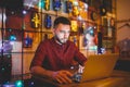 A young handsome Caucasian man with beard and toothy smile in a red checkered shirt is working behind a gray laptop Royalty Free Stock Photo