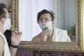 Young handsome caucasian man begins to shave with brush and foam, vintage style of old barber. Thoughtful serious look, Royalty Free Stock Photo