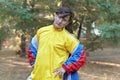 Young handsome caucasian man with bright freaky sportswear 70s style stands at a morning park. Stick in the mouth, golden glasses, Royalty Free Stock Photo