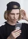 Young handsome caucasian man looks to the mobile phone screen like in mirror, getting up the hairs, or making selfie. Royalty Free Stock Photo