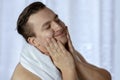 Young handsome caucasian man patted his cheeks after shaving, towel on shoulders. Caring face with cream or lotion, very pleased e Royalty Free Stock Photo