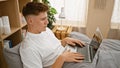 Young, handsome caucasian man sitting comfortably on his cozy bed, engrossed in online world through his laptop in the relaxing