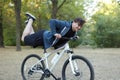 Young handsome caucasian man smiling performs stunt legs up on the bicycle at green park. Risky trick. White wireless earphones, c