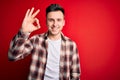 Young handsome caucasian man wearing casual modern shirt over red isolated background smiling positive doing ok sign with hand and Royalty Free Stock Photo