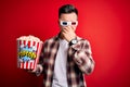 Young handsome caucasian man wearing 3d movie glasses and eating popcorn smelling something stinky and disgusting, intolerable