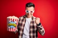 Young handsome caucasian man wearing 3d movie glasses and eating popcorn very happy and excited doing winner gesture with arms Royalty Free Stock Photo