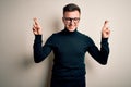 Young handsome caucasian man wearing glasses and casual sweater over isolated background gesturing finger crossed smiling with Royalty Free Stock Photo