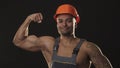 Muscular ripped African male builder in workwear and hardhat flexing muscles