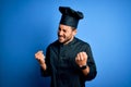 Young handsome chef man with beard wearing cooker uniform and hat over blue background very happy and excited doing winner gesture Royalty Free Stock Photo
