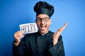 Young handsome chef man overworked wearing uniform and hat holding help paper message very happy and excited, winner expression