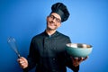 Young handsome chef man wearing cooker uniform and hat mixing using whisk and bowl with a happy face standing and smiling with a Royalty Free Stock Photo