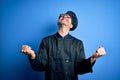 Young handsome chef man wearing cooker uniform and hat over isolated blue background very happy and excited doing winner gesture Royalty Free Stock Photo