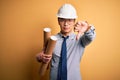 Young handsome chinese architect man wearing glasses and safety helmet holding blueprints with angry face, negative sign showing Royalty Free Stock Photo