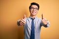 Young handsome chinese businessman wearing glasses and tie over yellow background approving doing positive gesture with hand, Royalty Free Stock Photo