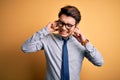 Young handsome chinese businessman wearing glasses and tie over yellow background covering ears with fingers with annoyed Royalty Free Stock Photo