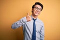 Young handsome chinese businessman wearing glasses and tie over yellow background doing happy thumbs up gesture with hand Royalty Free Stock Photo