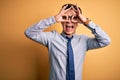 Young handsome chinese businessman wearing glasses and tie over yellow background doing ok gesture like binoculars sticking tongue Royalty Free Stock Photo