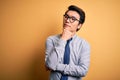 Young handsome chinese businessman wearing glasses and tie over yellow background with hand on chin thinking about question, Royalty Free Stock Photo