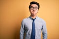 Young handsome chinese businessman wearing glasses and tie over yellow background puffing cheeks with funny face