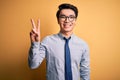 Young handsome chinese businessman wearing glasses and tie over yellow background showing and pointing up with fingers number two Royalty Free Stock Photo