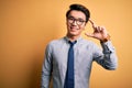 Young handsome chinese businessman wearing glasses and tie over yellow background smiling and confident gesturing with hand doing Royalty Free Stock Photo