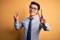 Young handsome chinese businessman wearing glasses and tie over yellow background smiling looking to the camera showing fingers Royalty Free Stock Photo