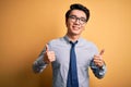 Young handsome chinese businessman wearing glasses and tie over yellow background success sign doing positive gesture with hand, Royalty Free Stock Photo