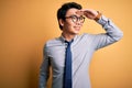 Young handsome chinese businessman wearing glasses and tie over yellow background very happy and smiling looking far away with Royalty Free Stock Photo