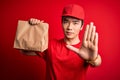 Young handsome chinese delivery man holding takeaway paper bag with food with open hand doing stop sign with serious and confident Royalty Free Stock Photo