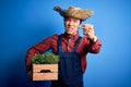 Young handsome chinese farmer man wearing apron and straw hat holding box with plants annoyed and frustrated shouting with anger, Royalty Free Stock Photo