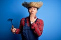 Young handsome chinese farmer man wearing apron and straw hat holding rake tool cover mouth with hand shocked with shame for