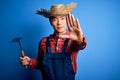 Young handsome chinese farmer man wearing apron and straw hat holding rake tool with open hand doing stop sign with serious and Royalty Free Stock Photo