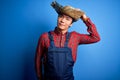 Young handsome chinese farmer man wearing apron and straw hat over blue background confuse and wonder about question