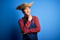 Young handsome chinese farmer man wearing apron and straw hat over blue background with hand on chin thinking about question,