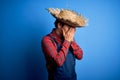 Young handsome chinese farmer man wearing apron and straw hat over blue background with sad expression covering face with hands Royalty Free Stock Photo