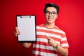 Young handsome chinese inspector man wearing glasses holding clipboard checklist very happy pointing with hand and finger Royalty Free Stock Photo