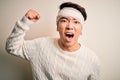 Young handsome chinese man injured for accident wearing bandage and strips on head angry and mad raising fist frustrated and