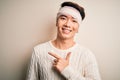Young handsome chinese man injured for accident wearing bandage and strips on head cheerful with a smile on face pointing with