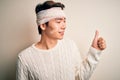 Young handsome chinese man injured for accident wearing bandage and strips on head Looking proud, smiling doing thumbs up gesture
