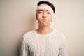 Young handsome chinese man injured for accident wearing bandage and strips on head puffing cheeks with funny face