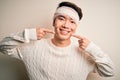 Young handsome chinese man injured for accident wearing bandage and strips on head smiling cheerful showing and pointing with
