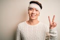 Young handsome chinese man injured for accident wearing bandage and strips on head smiling looking to the camera showing fingers Royalty Free Stock Photo