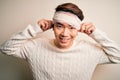 Young handsome chinese man injured for accident wearing bandage and strips on head Smiling pulling ears with fingers, funny