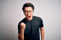 Young handsome chinese man wearing black t-shirt and glasses over white background angry and mad raising fist frustrated and Royalty Free Stock Photo