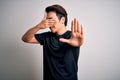 Young handsome chinese man wearing black t-shirt and glasses over white background covering eyes with hands and doing stop gesture Royalty Free Stock Photo