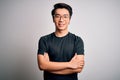Young handsome chinese man wearing black t-shirt and glasses over white background happy face smiling with crossed arms looking at Royalty Free Stock Photo