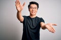 Young handsome chinese man wearing black t-shirt and glasses over white background looking at the camera smiling with open arms Royalty Free Stock Photo