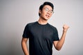 Young handsome chinese man wearing black t-shirt and glasses over white background smiling with happy face looking and pointing to Royalty Free Stock Photo